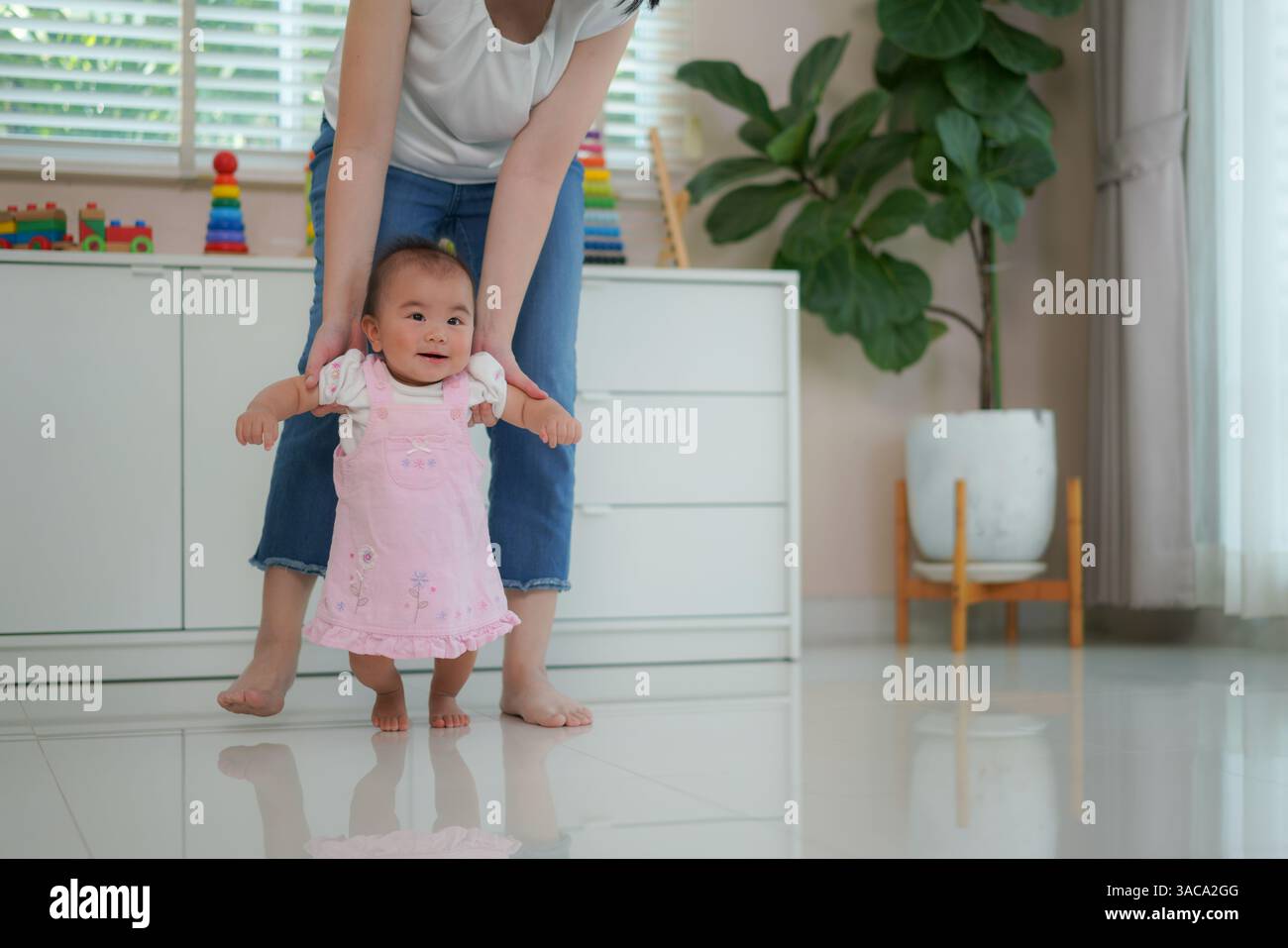 Madre che sostiene il suo bambino mentre si esercitano in piedi e camminano prima pietra miliare dello sviluppo e il legame amorevole tra genitore e figlio Foto Stock