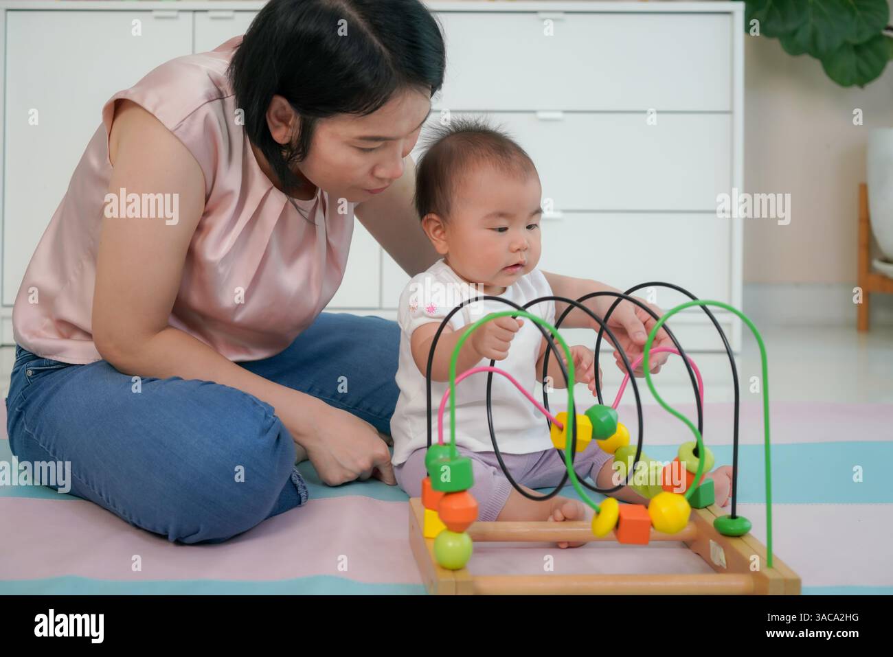 La madre aiuta il suo bambino a navigare in un labirinto di perle di legno dai colori vivaci mette in risalto l'apprendimento precoce e lo sviluppo delle abilità motorie Foto Stock
