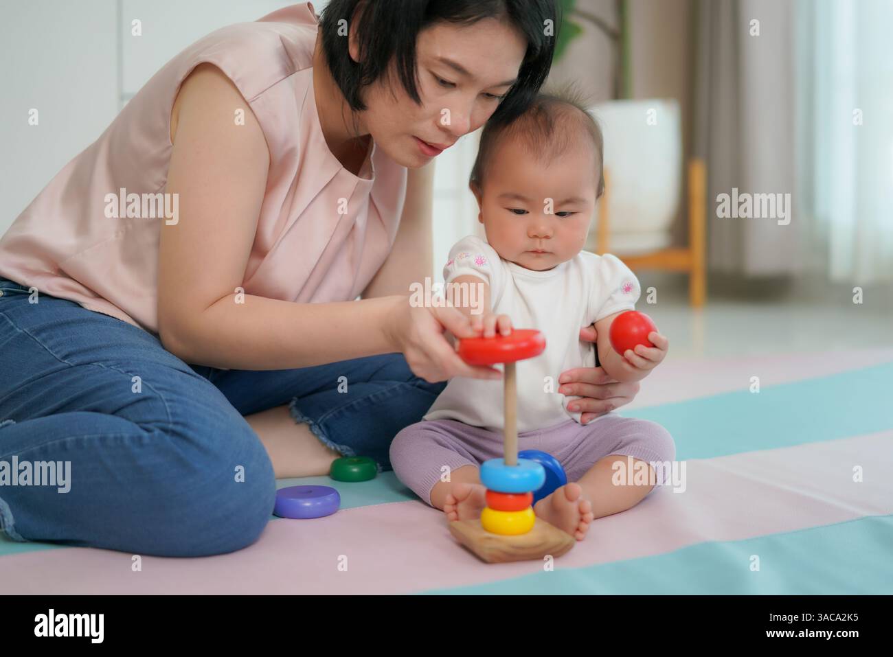 Una madre che guida il suo bambino a impilare anelli di legno colorati su un giocattolo a forma di piolo mostra lo sviluppo precoce delle abilità. Foto Stock