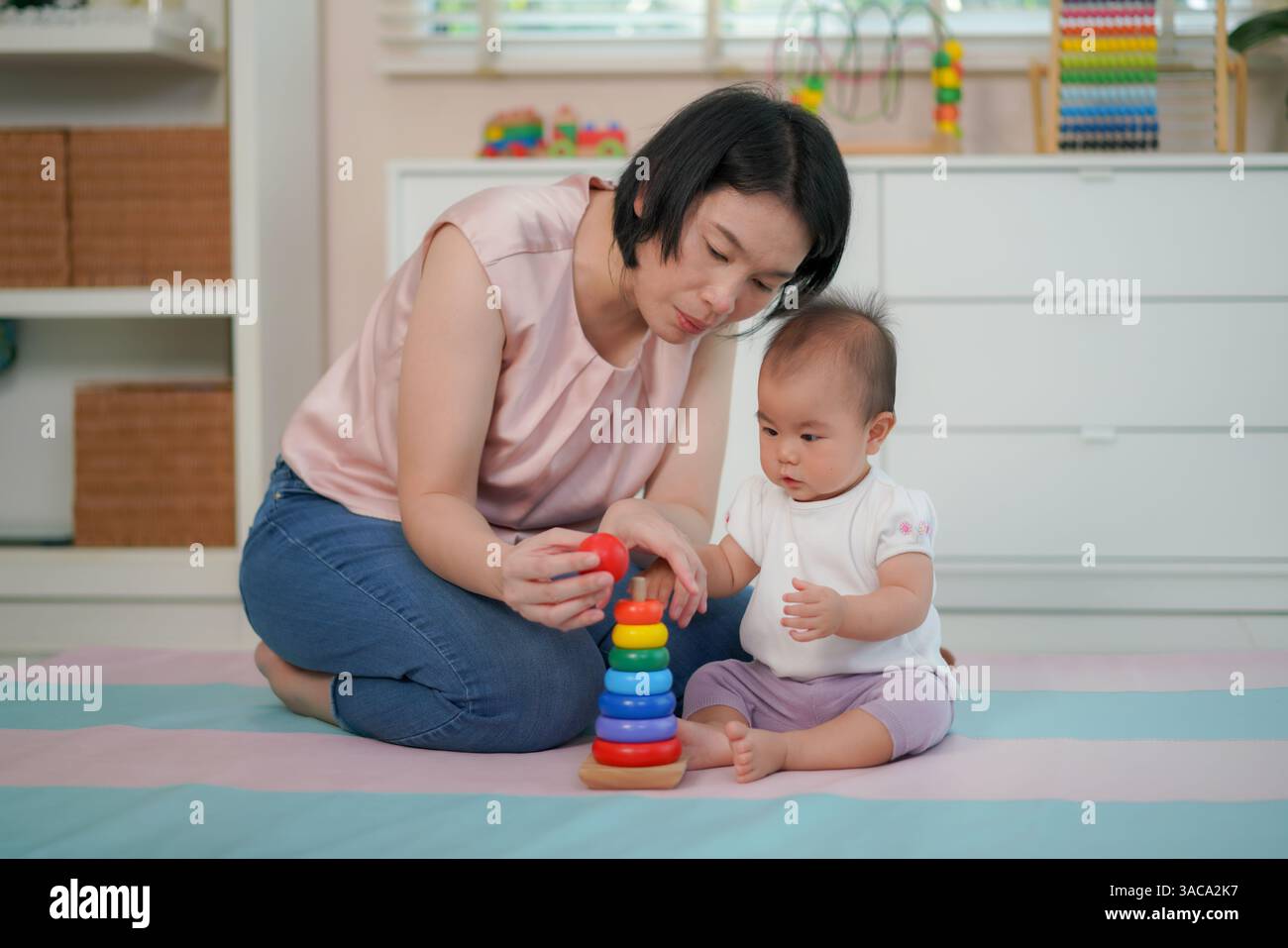 Una madre che guida il suo bambino a impilare anelli di legno colorati su un giocattolo a forma di piolo mostra lo sviluppo precoce delle abilità. Foto Stock