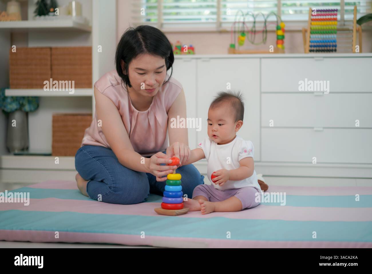 Una madre che guida il suo bambino a impilare anelli di legno colorati su un giocattolo a forma di piolo mostra lo sviluppo precoce delle abilità. Foto Stock