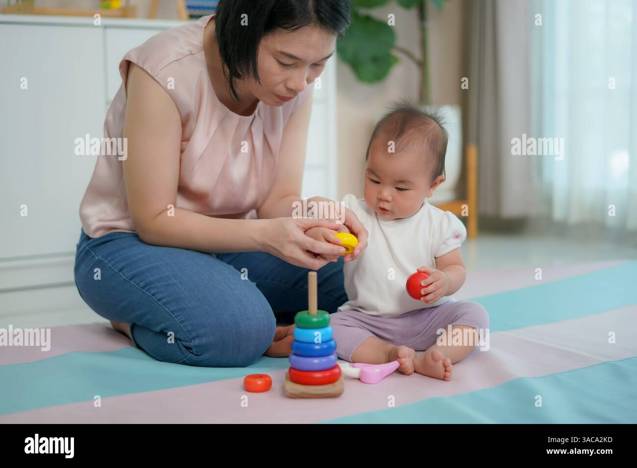 Una madre che guida il suo bambino a impilare anelli di legno colorati su un giocattolo a forma di piolo mostra lo sviluppo precoce delle abilità. Foto Stock