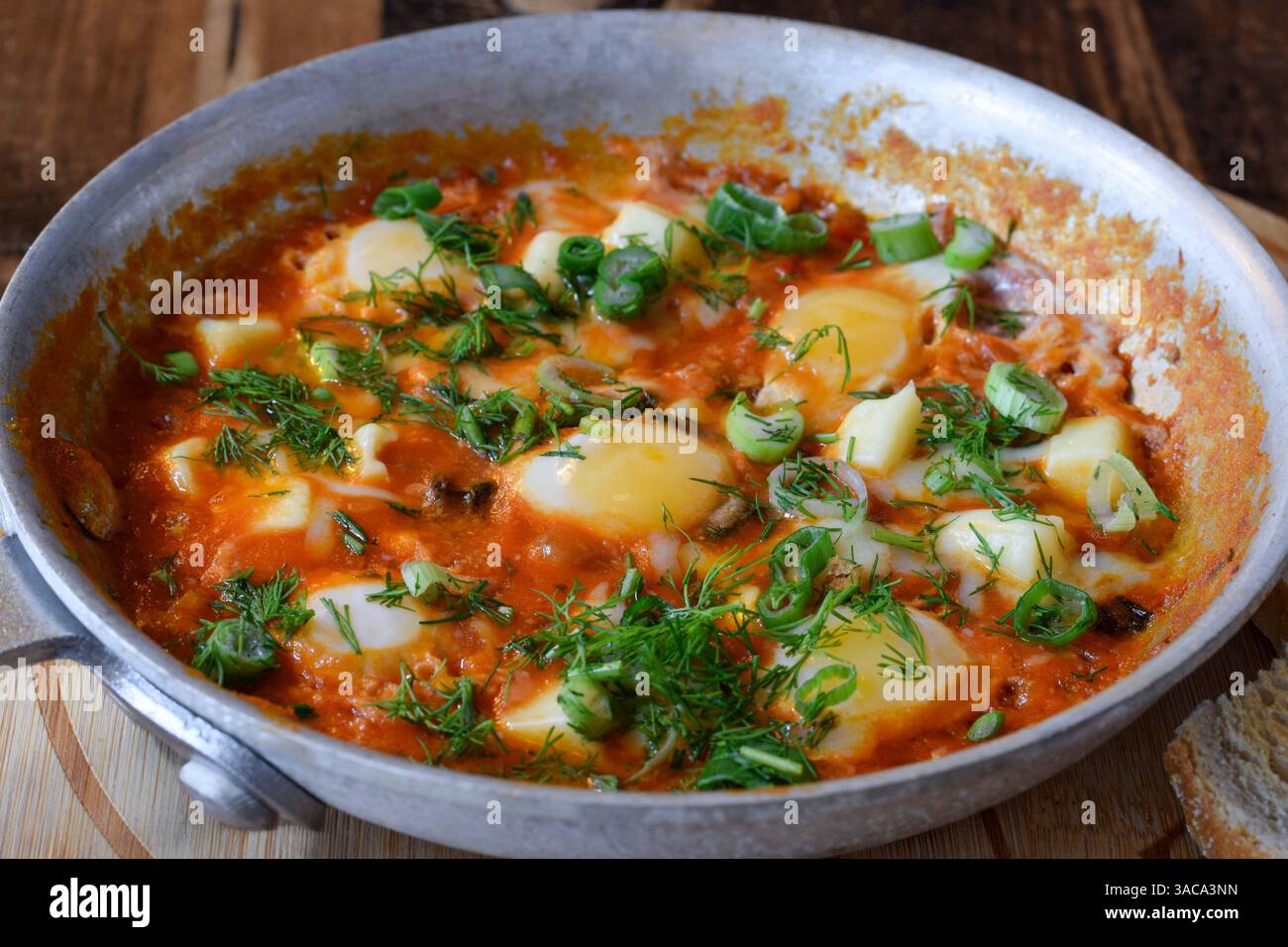 Shakshuka per la colazione da vicino con aneto fresco e cipolle verdi in padella su un tavolo di legno Foto Stock