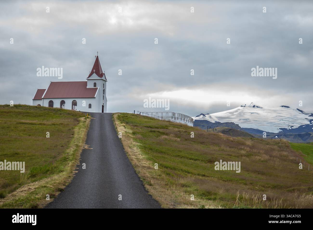 Una strada che porta alla chiesa di Ingjaldsholl con montagne innevate sullo sfondo a Hellisandur, penisola di Snaefellsnes, Islanda. Foto Stock