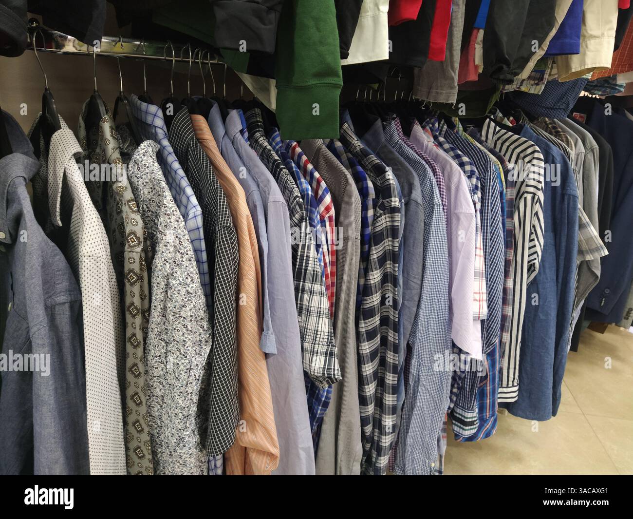 Vestiti appesi su grucce. Assortimento di negozio di seconda mano. Camicie da uomo appese su una rastrelliera, pronte per la vendita ai clienti. Risparmiare denaro in crisi. Economico s Foto Stock