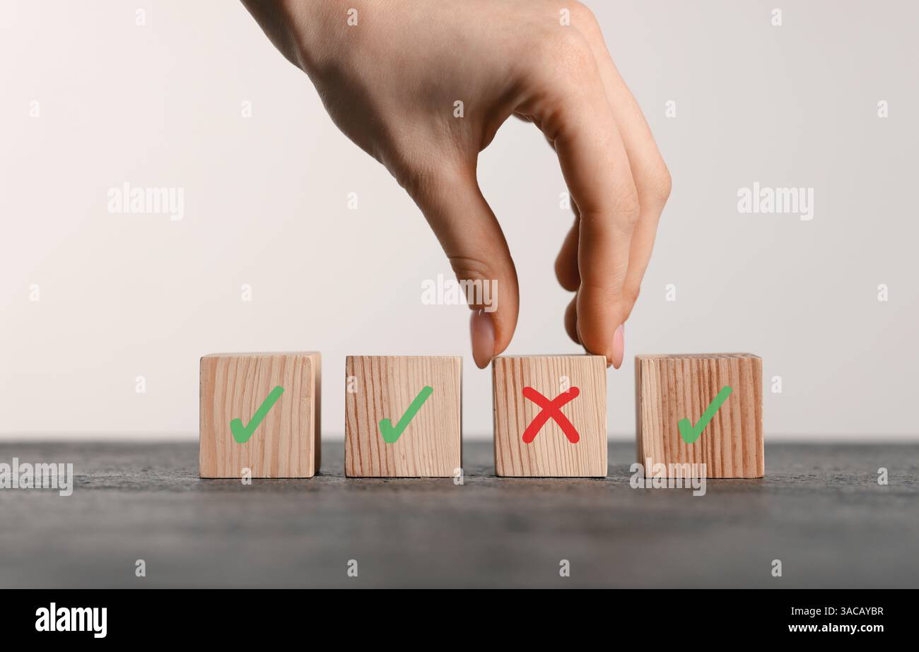 Rifiutato. Donna che sceglie cubo con croce tra gli altri con segni di spunta a tavola, primo piano Foto Stock