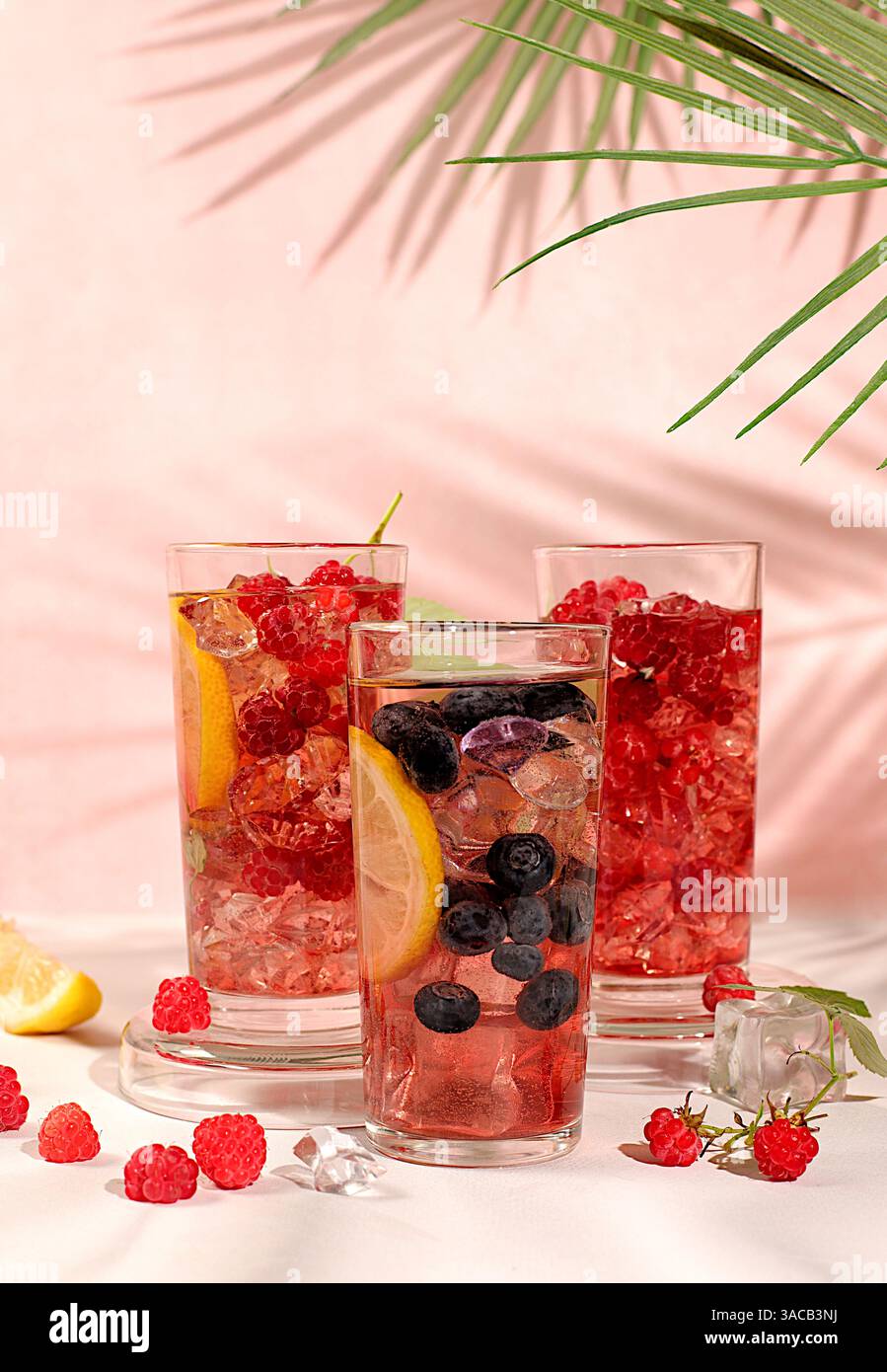 Natura morta moderna con succo di frutti di bosco, lamponi, mirtilli, ribes rossi e arance su un elegante tavolo da cucina con ombre lunghe e dure. Disintossicazione minima Foto Stock