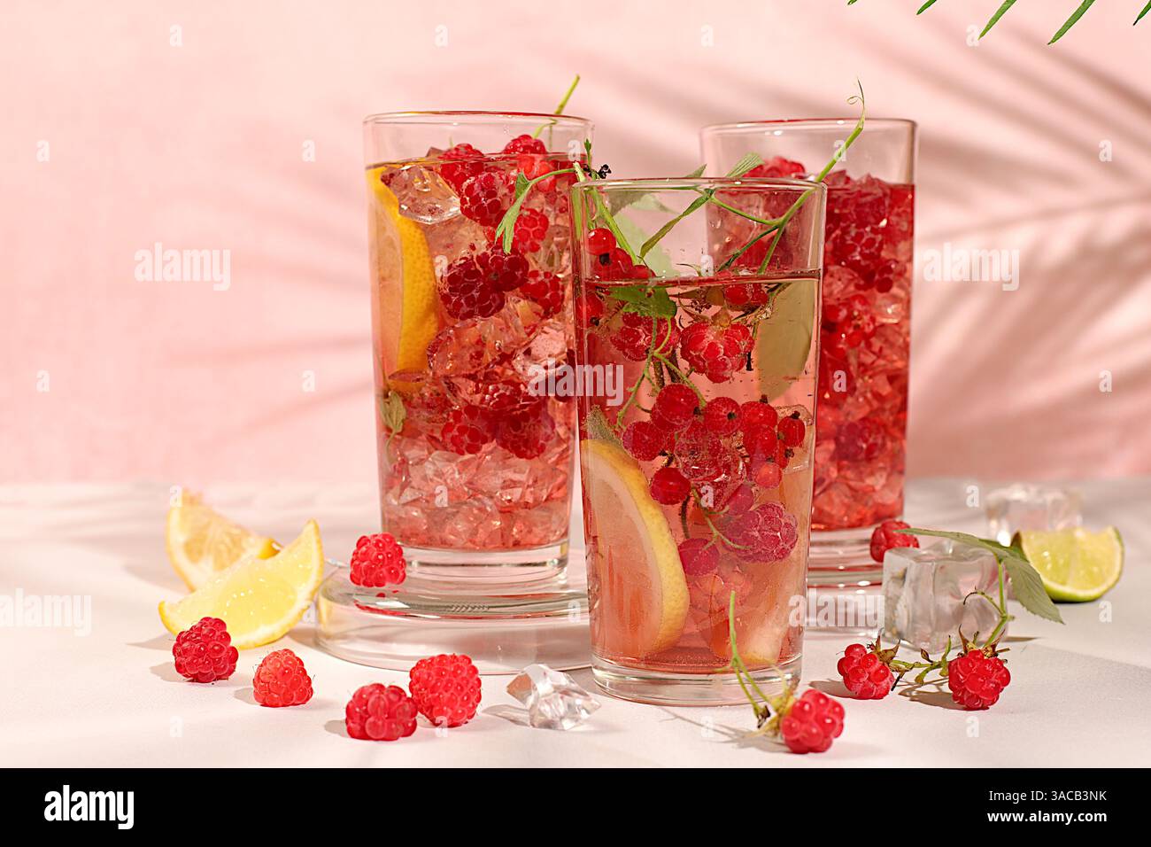 Natura morta moderna con succo di frutti di bosco, lamponi, ribes rosso, menta e arance su un elegante tavolo da cucina con ombre lunghe e dure. Dieta disintossicante minima co Foto Stock