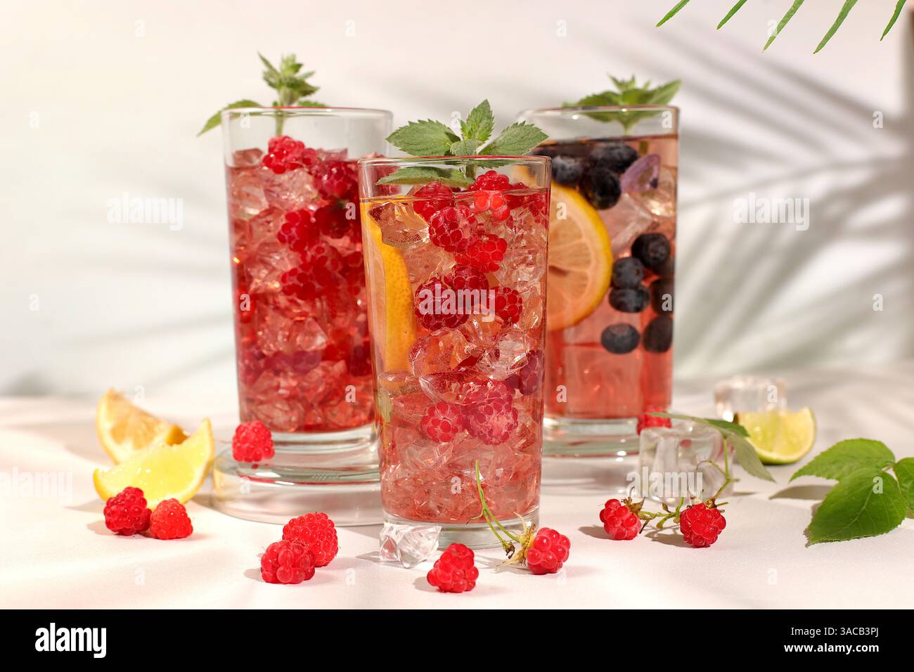 Natura morta moderna con succo di frutti di bosco, lamponi, mirtilli, ribes rossi e arance su un elegante tavolo da cucina con ombre lunghe e dure. Disintossicazione minima Foto Stock