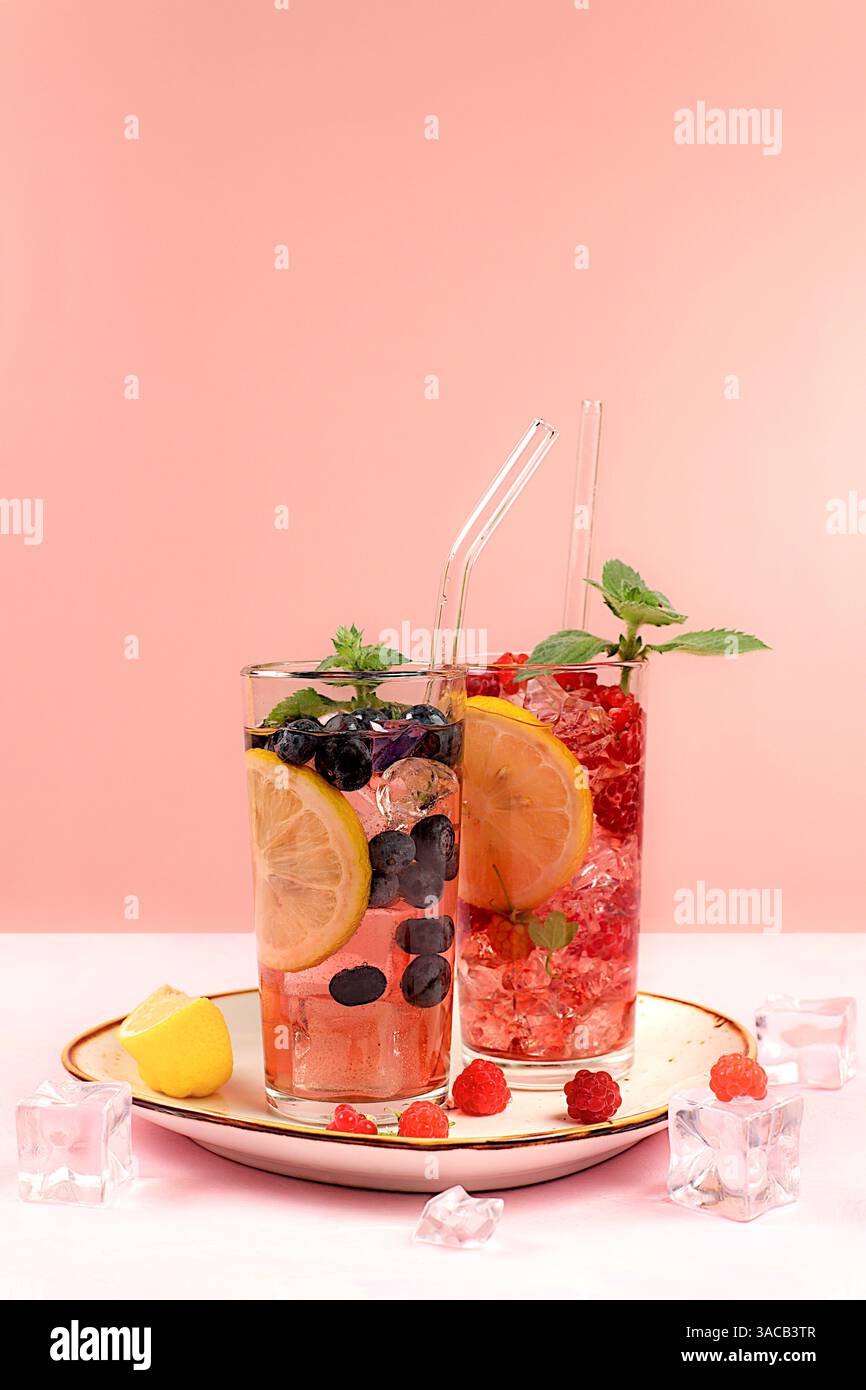 Natura morta moderna con succo di frutti di bosco, lamponi, mirtilli, ribes rossi e arance su un elegante tavolo da cucina con ombre lunghe e dure. Disintossicazione minima Foto Stock