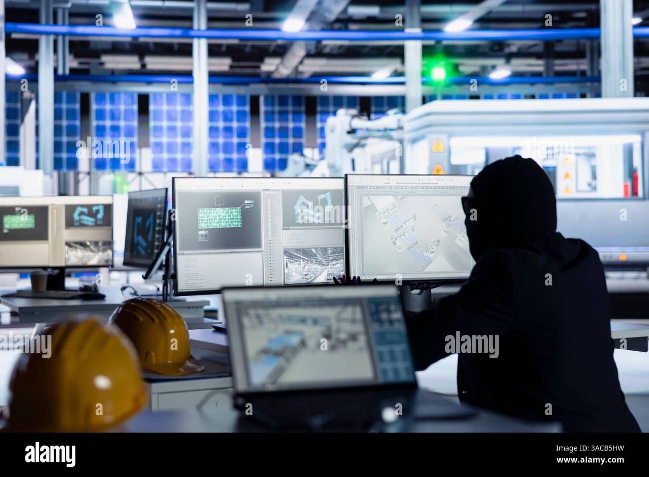 Il lavoratore mascherato in una fabbrica di fotovoltaico commette spionaggio aziendale, osservando i progetti su PC e rubando tecnologia proprietaria. L'uomo ignora la sicurezza degli impianti a pannelli solari per copiare i segreti commerciali Foto Stock