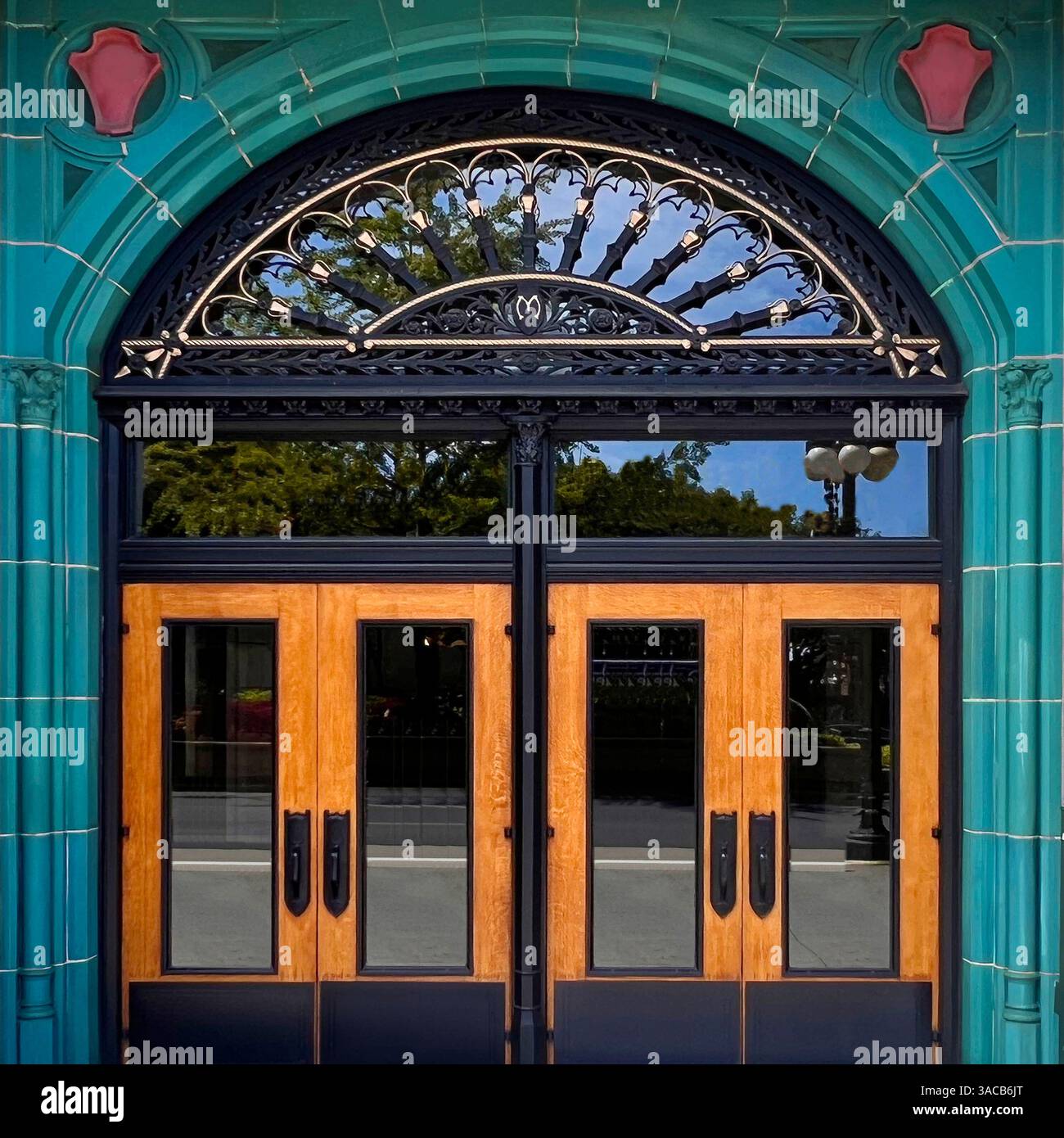 Suggestive porte doppie in legno con finiture nere e un fanlight decorato si trovano all'interno di una vivace arcata con piastrelle color verde acqua. - Immagine stock catturata con smartphone