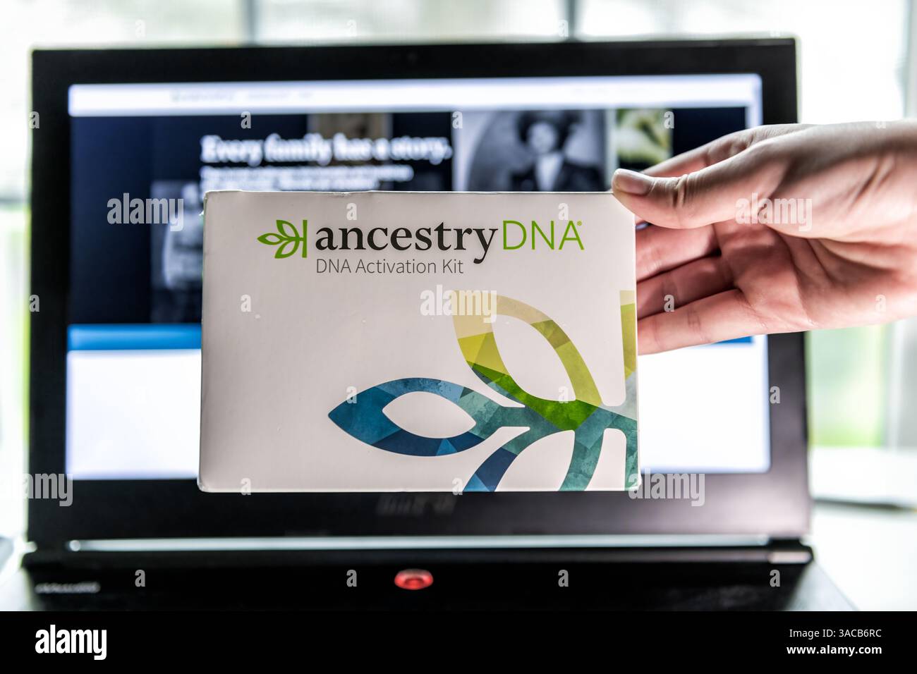 Fairfax, USA - 24 marzo 2023: Scatola kit di attivazione DNA AncestryDNA per il test della saliva genetica, mano che tiene primo piano da un computer portatile in background Foto Stock