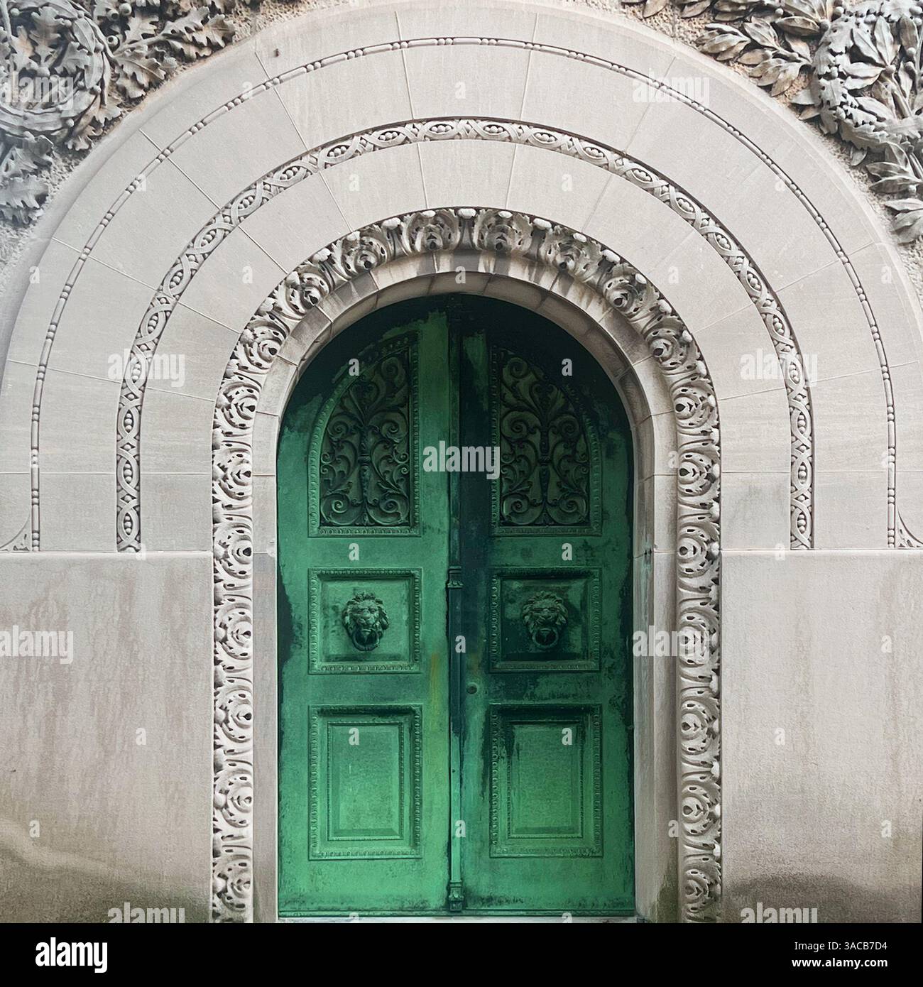 Una porta in bronzo verde riccamente dettagliata con battitori a testa di leone incastonata in un arco di pietra ornato segna l'ingresso di una tomba storica. - Immagine stock catturata con smartphone