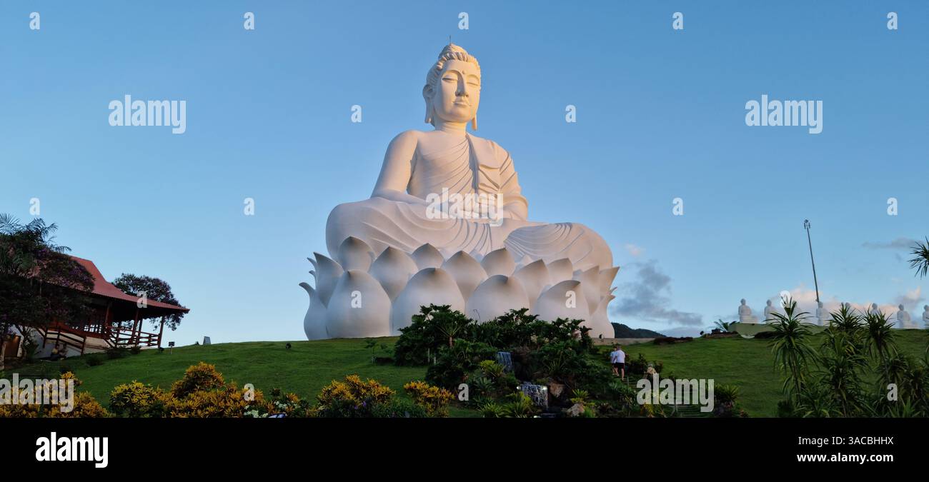 Mentre l'ultima luce del giorno lascia il posto al crepuscolo, una statua bianca di Buddha serena e maestosa si trova in una tranquilla cima a una collina verdeggiante. - Immagine stock catturata con smartphone