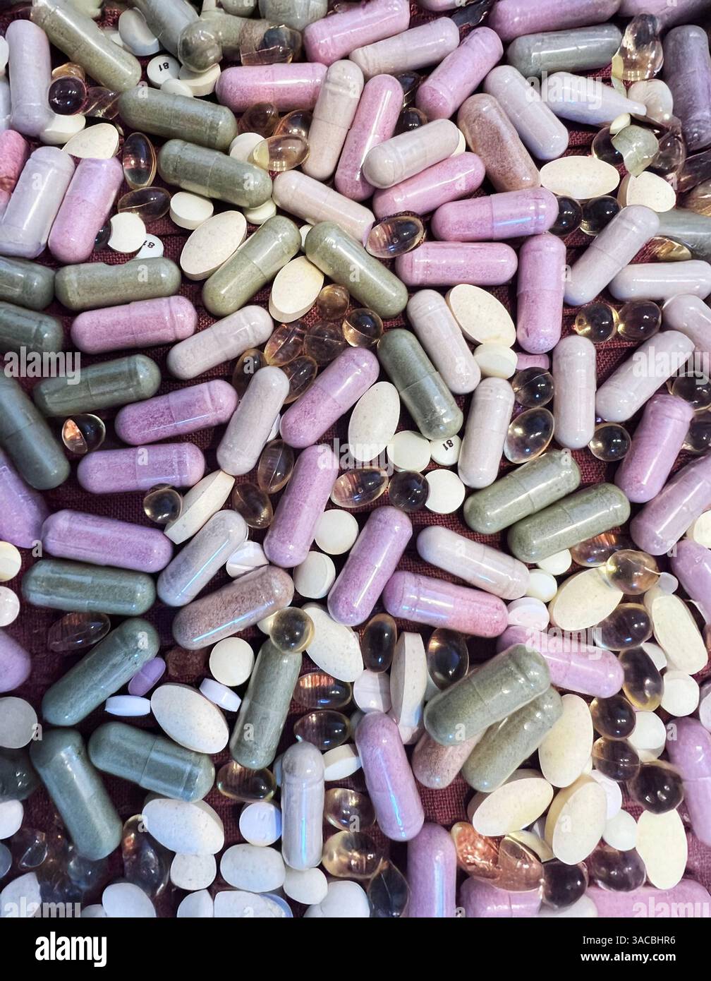 Numerosi integratori alimentari in vari colori e forme si trovano sparsi su una superficie, tra cui capsule, gel morbidi e compresse. Il riflesso dell'assortimento Foto Stock