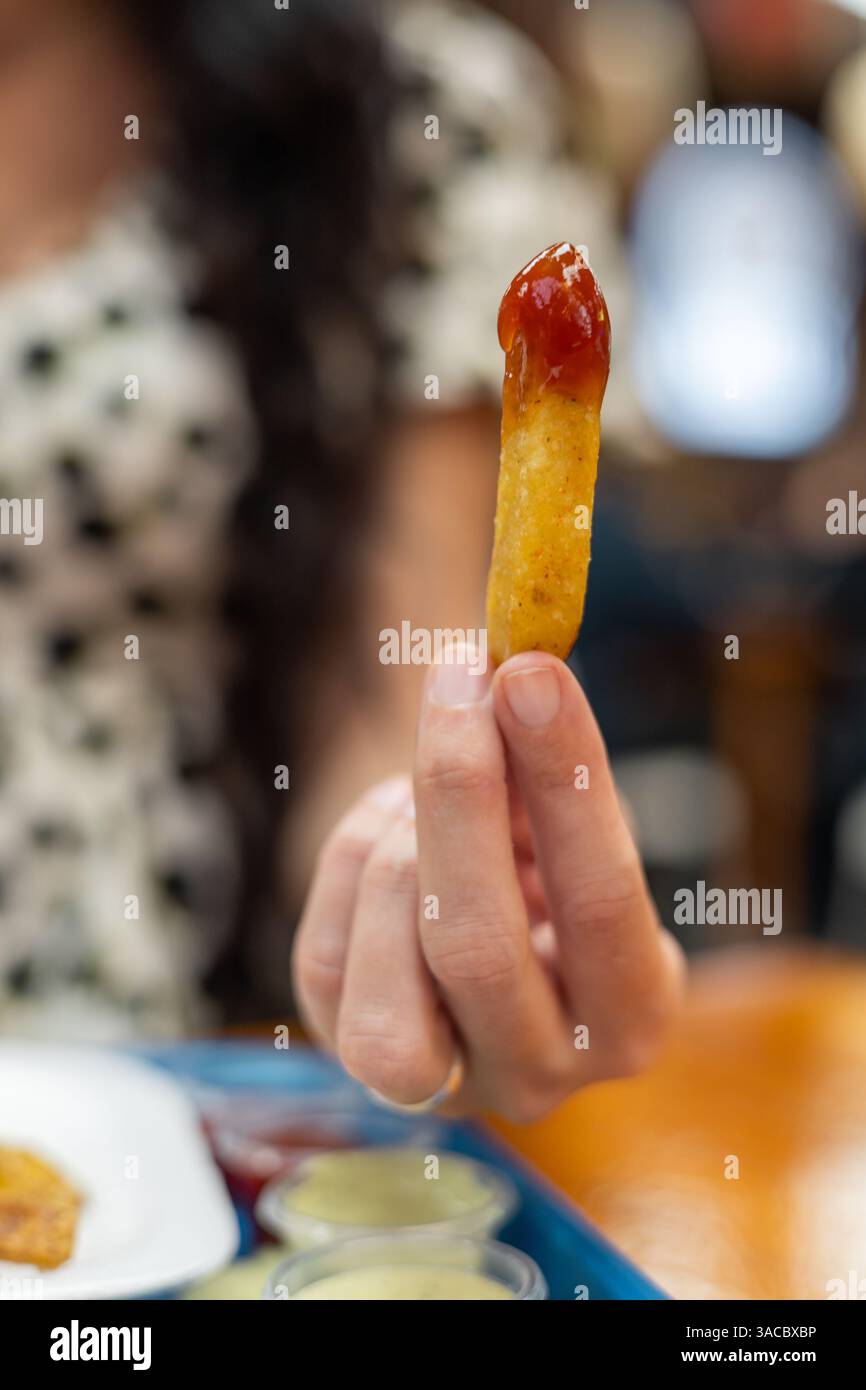 Un braccio si allunga per una frittura croccante, immersa nel ketchup, catturando l'essenza del piacere in un'esperienza culinaria informale. Foto Stock