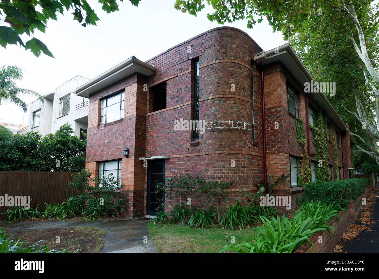 Fronte di un vecchio edificio di appartamenti a due piani in mattoni rossi nella periferia di Melbourne, con lussureggiante giardino frontale in primo piano Foto Stock