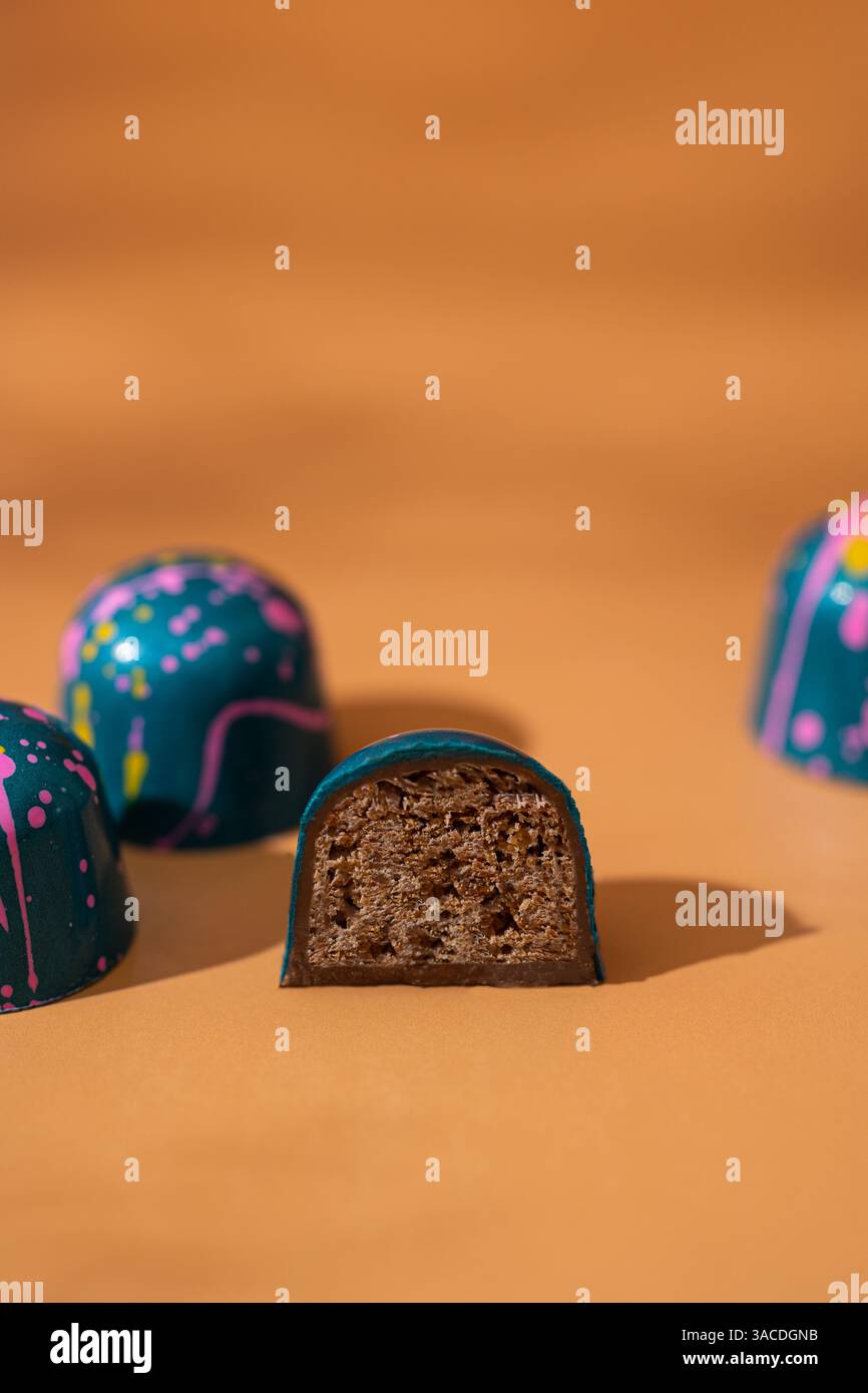 Funky Bonbons al cioccolato con stampa e riempimento a spruzzo di colore – primo piano su sfondo arancione Foto Stock