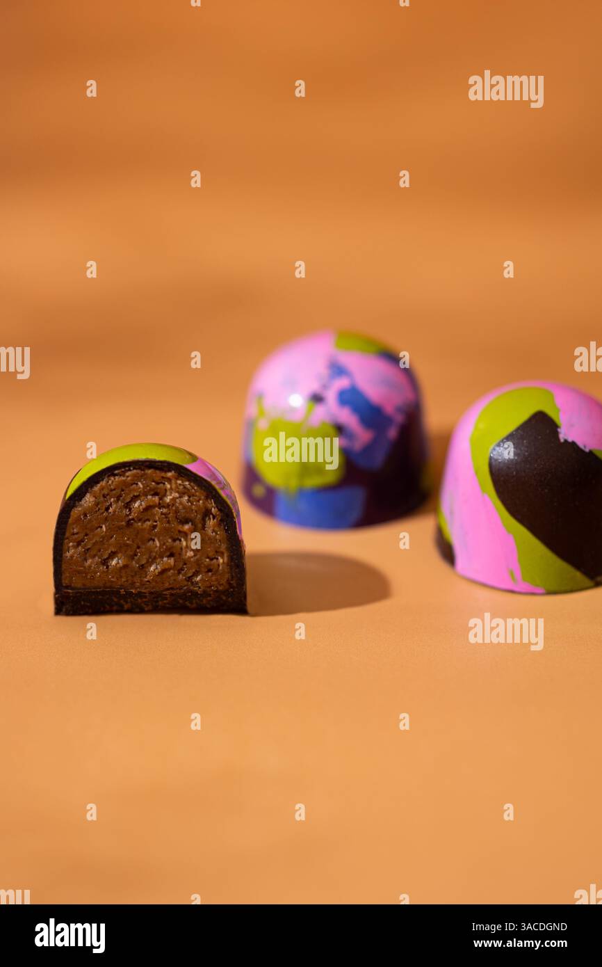 Funky Bonbons al cioccolato con stampa e riempimento a spruzzo di colore – primo piano su sfondo arancione Foto Stock
