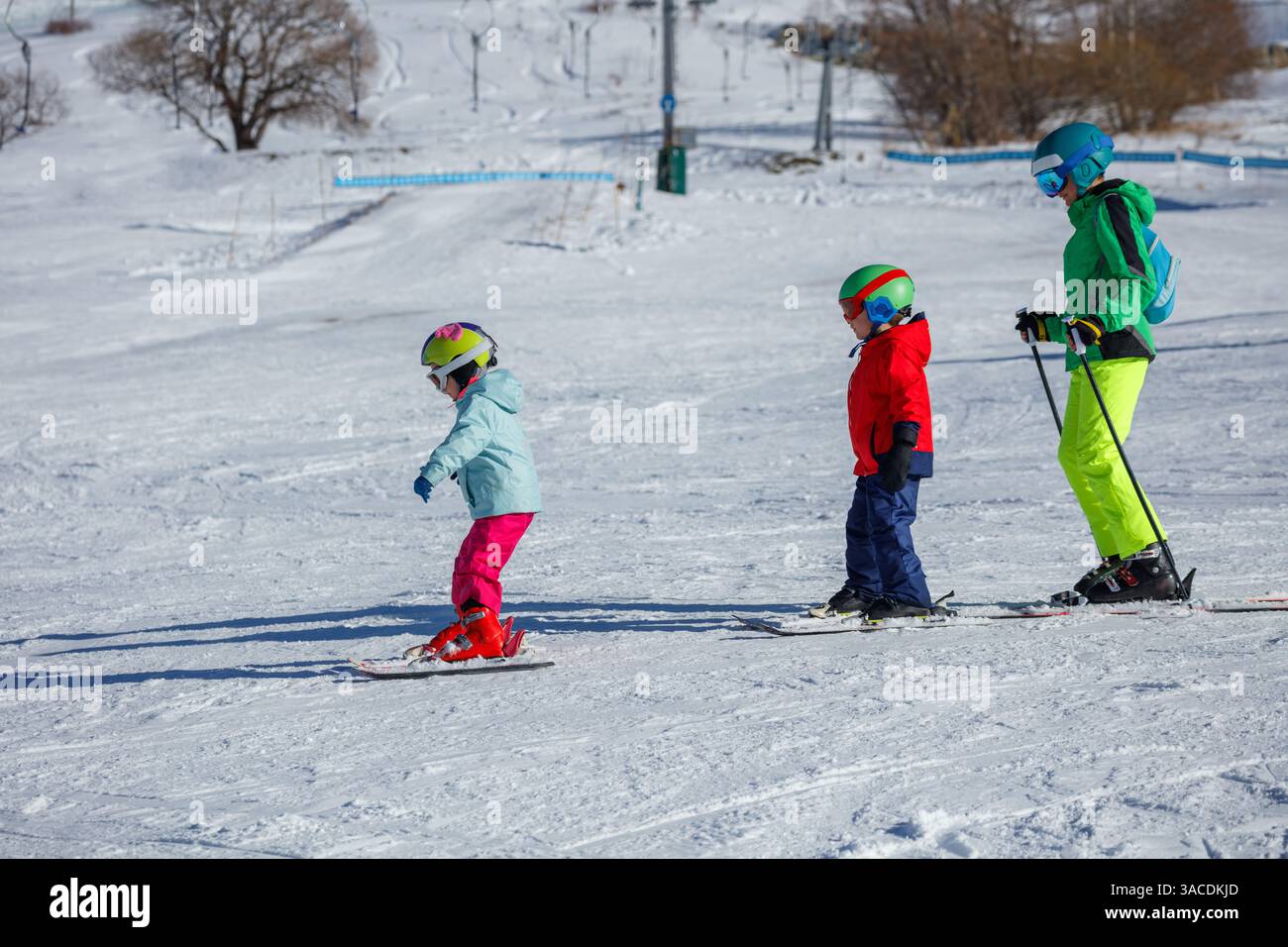 I bambini in abiti da sci brillanti scivolano giù da una collina innevata presso il resort Foto Stock