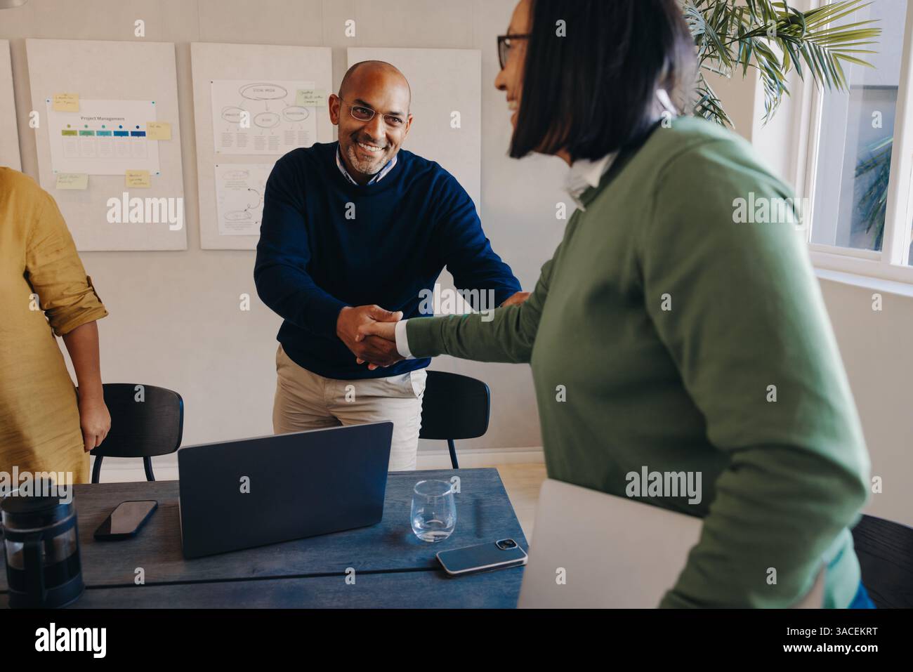 Due professionisti si salutano con una stretta di mano durante una riunione collaborativa in un ufficio, mostrando il lavoro di squadra e la comunicazione. Foto Stock