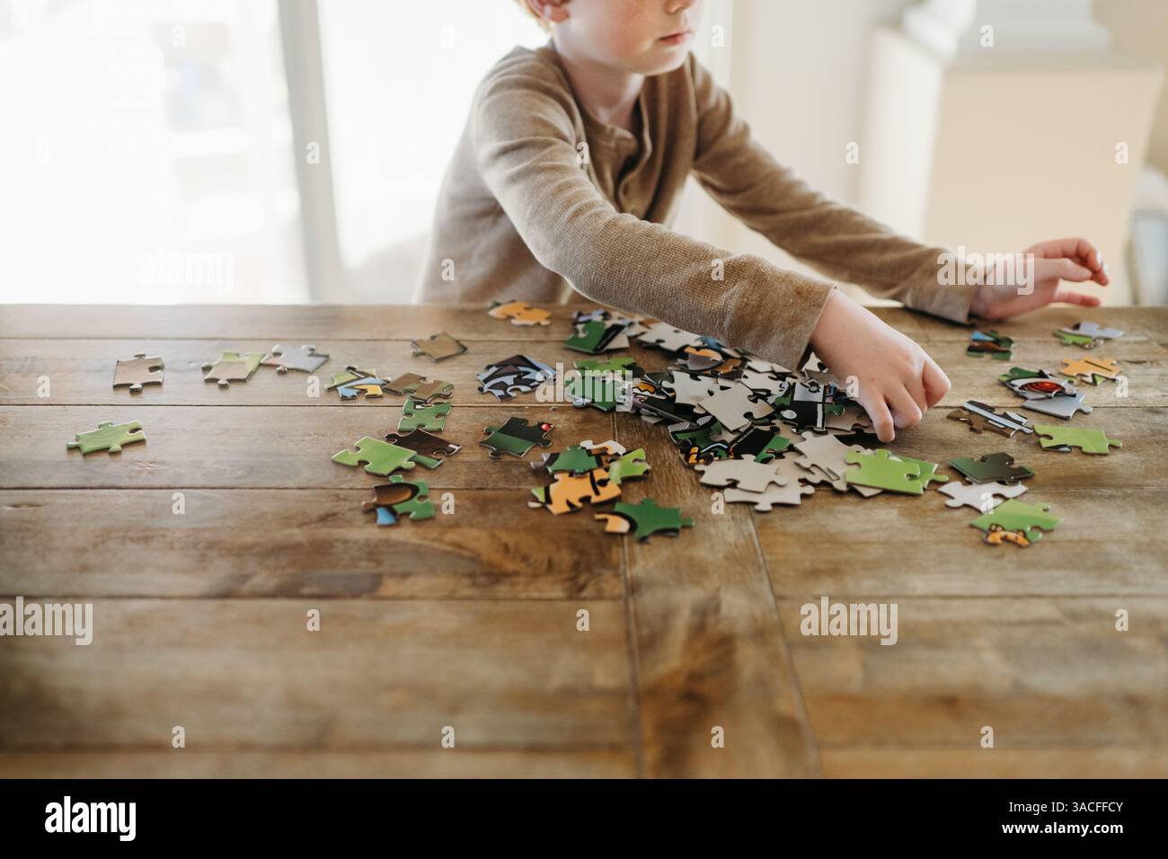 Ragazzo che ordina i pezzi del puzzle al tavolo da cucina a casa Foto Stock