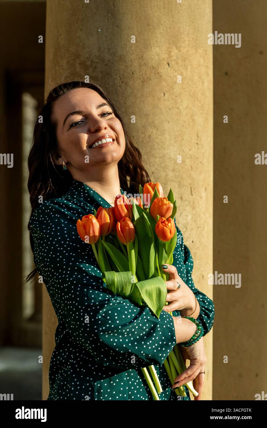 Donna felice che abbraccia i tulipani contro la luce calda del sole Foto Stock