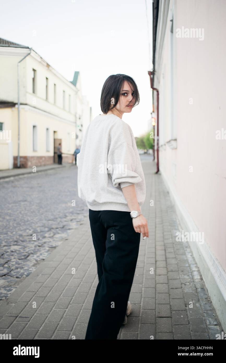 Donna elegante con una felpa leggera che percorre una tranquilla strada della città Foto Stock