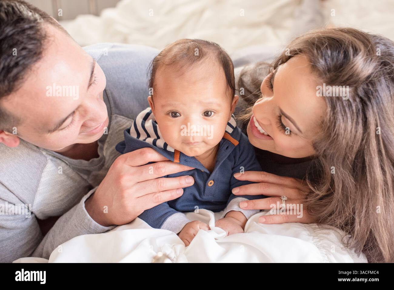 I genitori sorridono al neonato sul letto Foto Stock