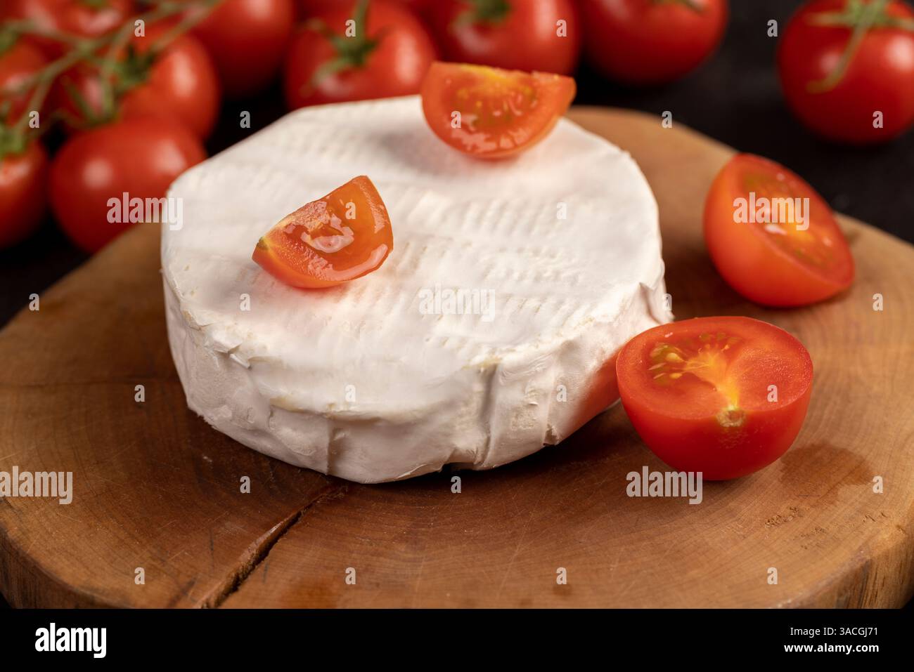 un formaggio con muffa e pomodori, un pezzo di formaggio morbido maturo e alcuni piccoli pomodori rotondi rossi sul tavolo, da vicino Foto Stock