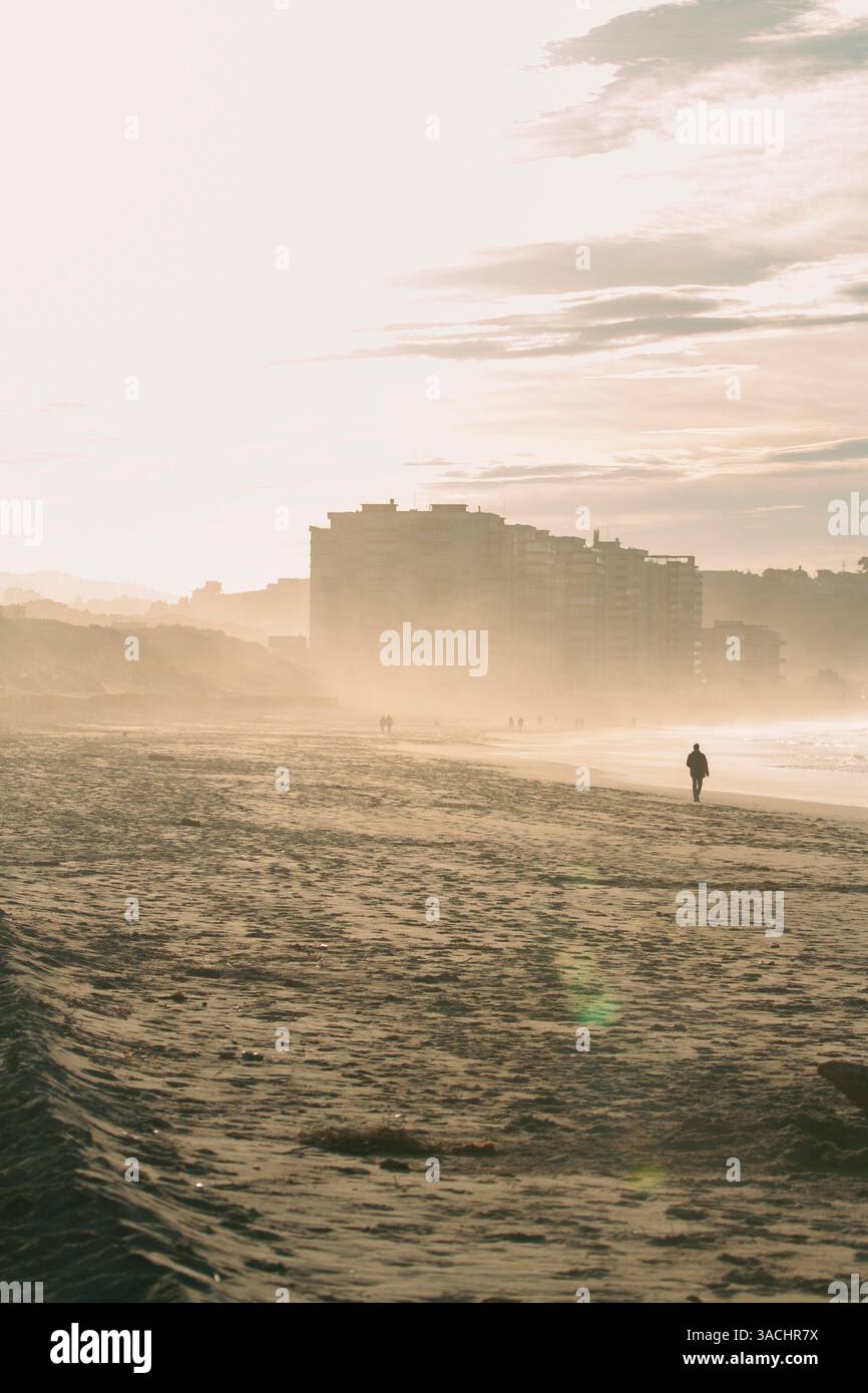 Uomo in piedi nella nebbia marina di fronte a una città, Salinas, Spagna Foto Stock