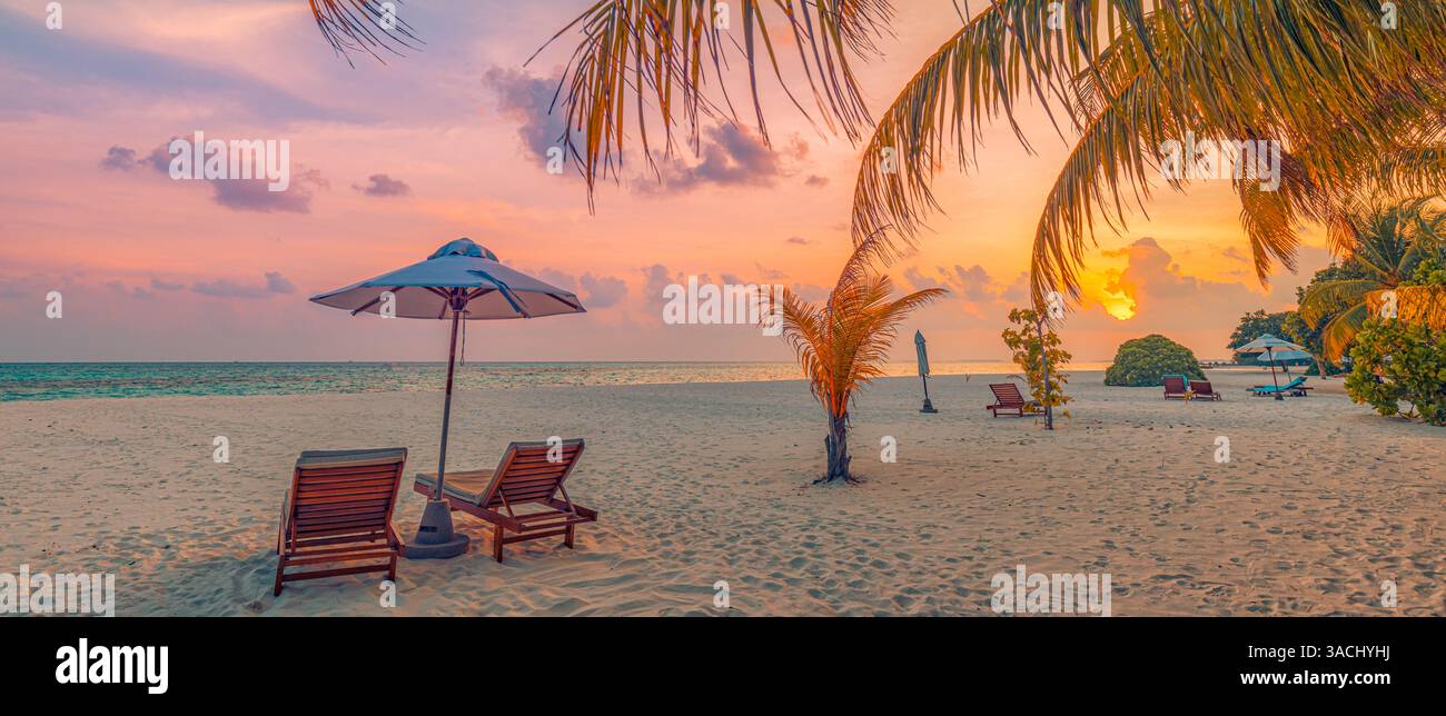 Lussuoso resort sulla spiaggia con vista del tramonto, sedie a sdraio, ombrelloni, palme, paesaggio mozzafiato, perfetto per una tranquilla fuga tropicale estiva. Sfondo destinazione esotica Foto Stock