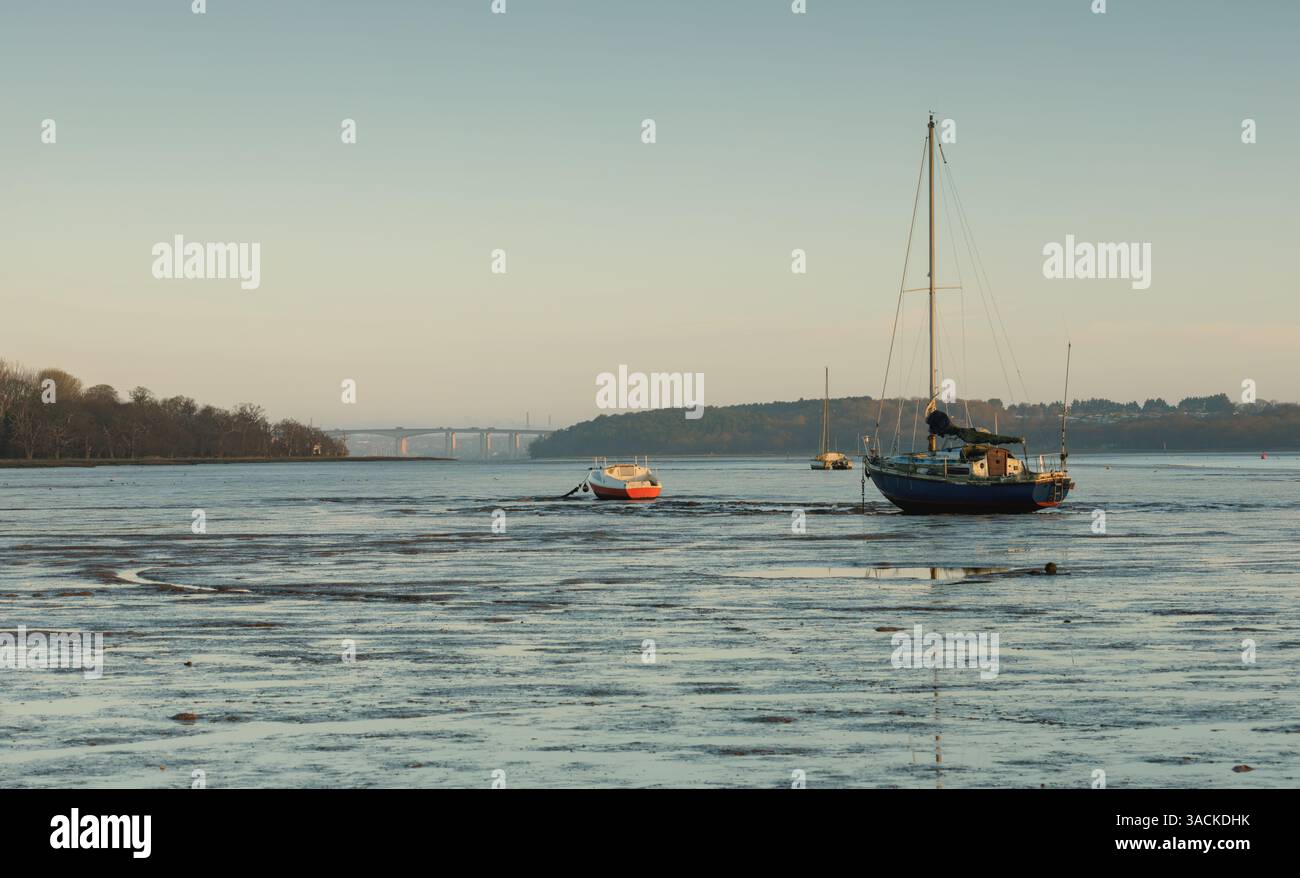 Barche ancorate su distese di fango a pin Mill, Suffolk, con il ponte Orwell in lontananza. Foto Stock