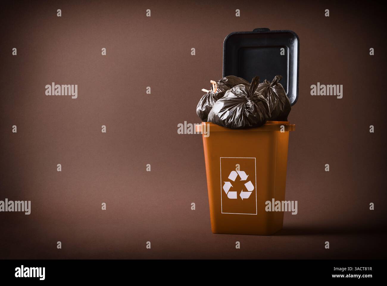 Concetto di riciclaggio dei rifiuti organici con un contenitore marrone con il simbolo di riciclaggio riempito con sacchetti marrone scuro isolati su sfondo marrone. Vista frontale. Foto Stock