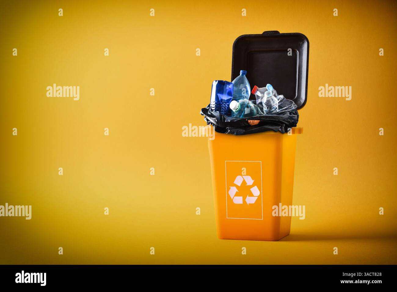 Concetto di riciclaggio con un contenitore giallo riempito di plastica e imballaggio con il simbolo di riciclaggio su sfondo giallo. Vista frontale. Foto Stock