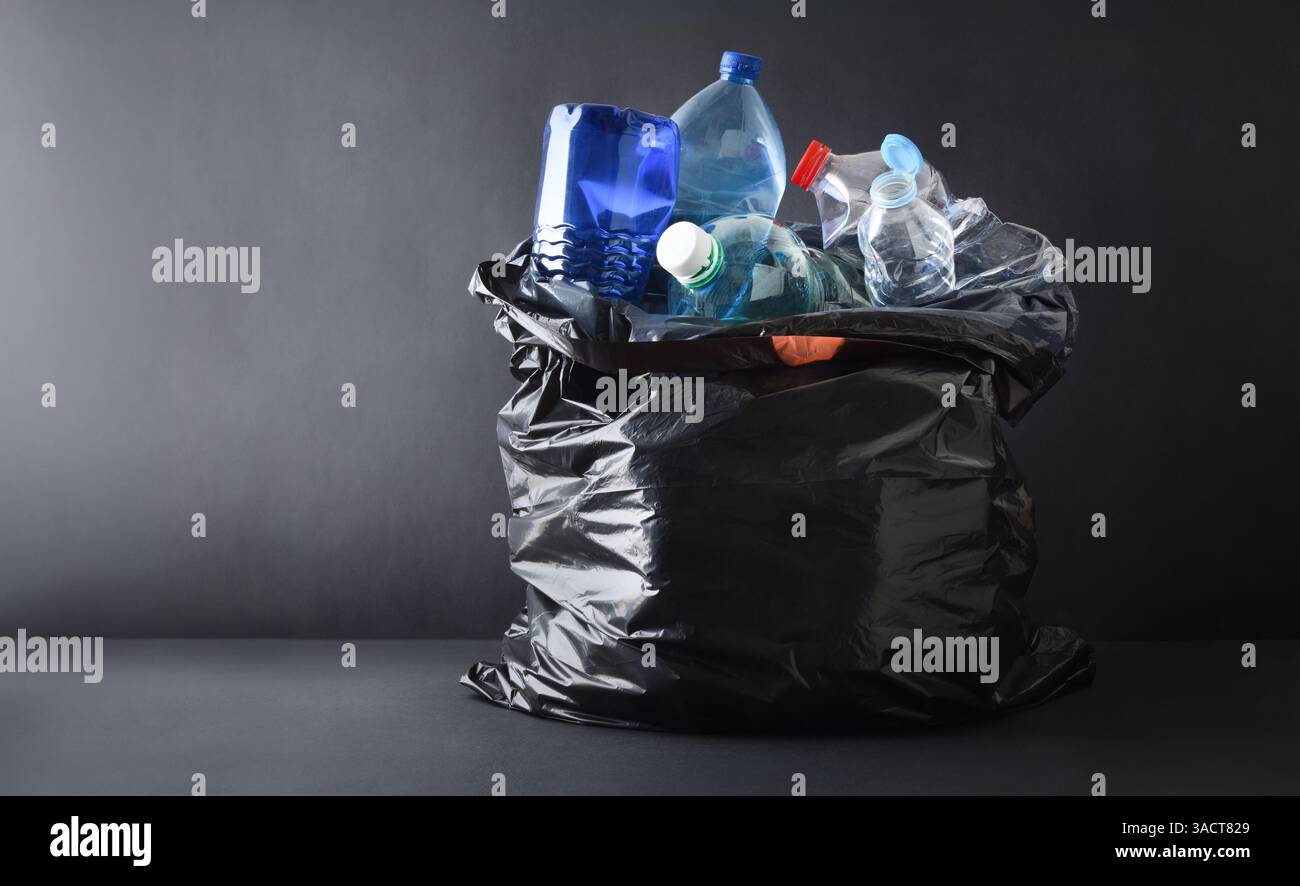 Sfondo con dettagli in sacchetto per rifiuti in plastica nera pieno di contenitori in plastica isolati su sfondo scuro e base. Vista frontale. Foto Stock