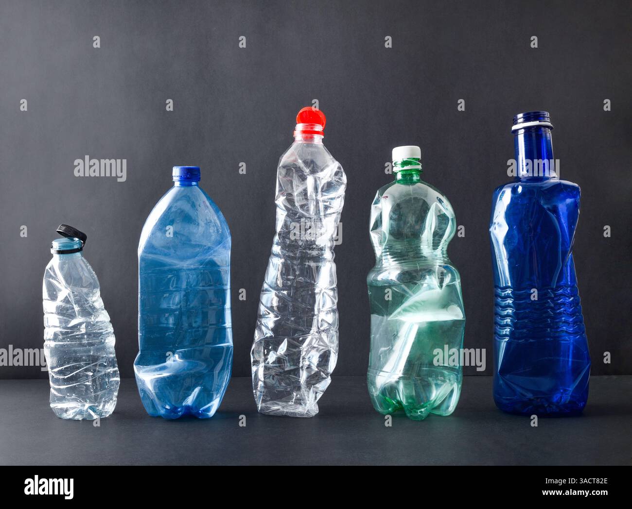 Concetto di inquinamento e riciclaggio della plastica con fila di bottiglie di plastica su base nera isolate su sfondo nero. Vista frontale. Foto Stock
