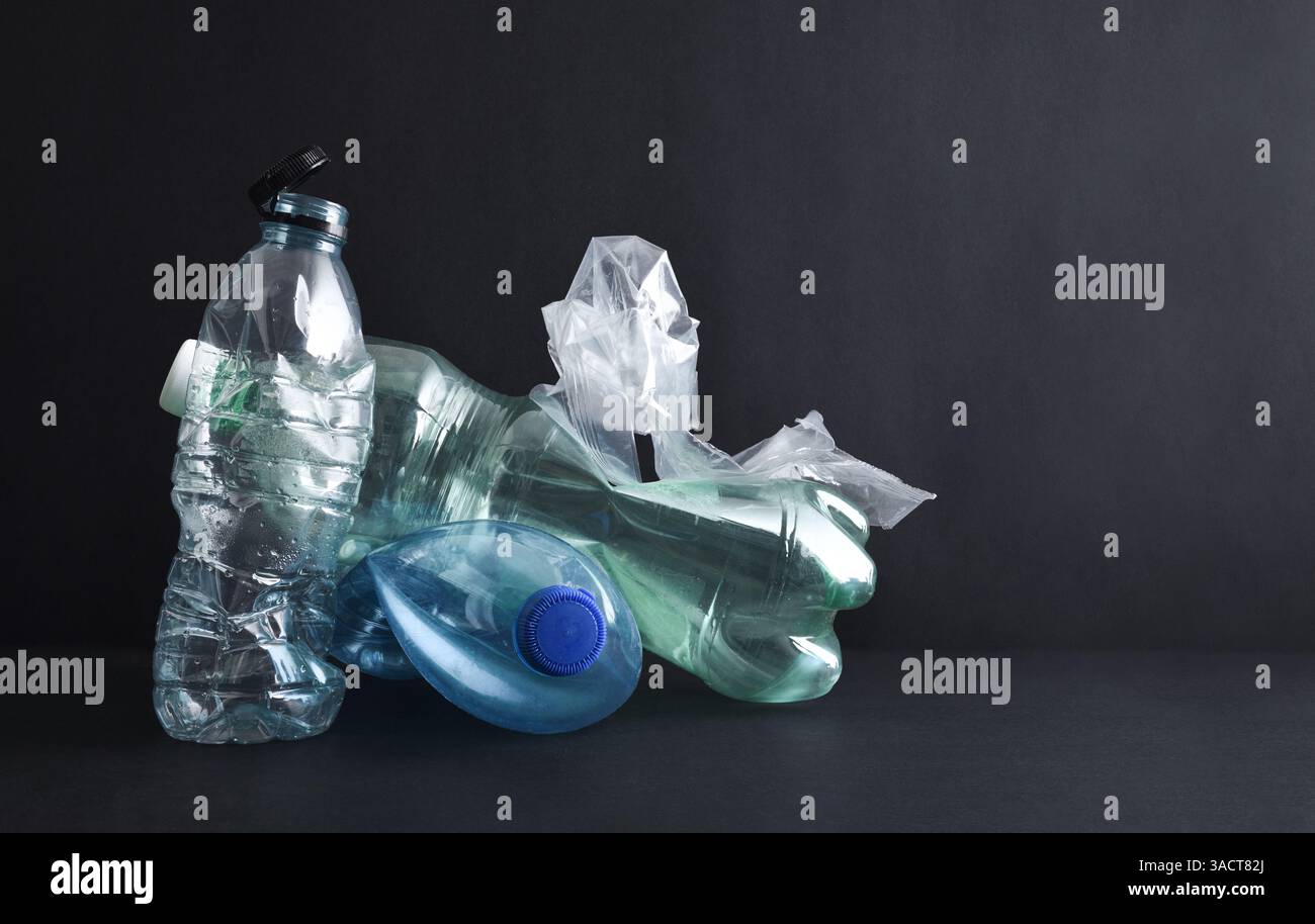 Concetto di inquinamento e riciclaggio della plastica con pile di bottiglie e contenitori in plastica su base nera isolati su sfondo nero. Vista frontale. Foto Stock