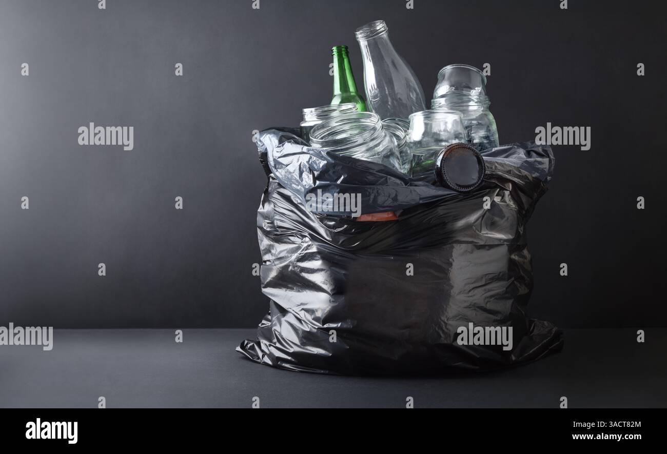 Sfondo con dettagli in sacchetto per rifiuti in plastica nera pieno di contenitori in vetro isolati su sfondo scuro e base. Vista frontale. Foto Stock