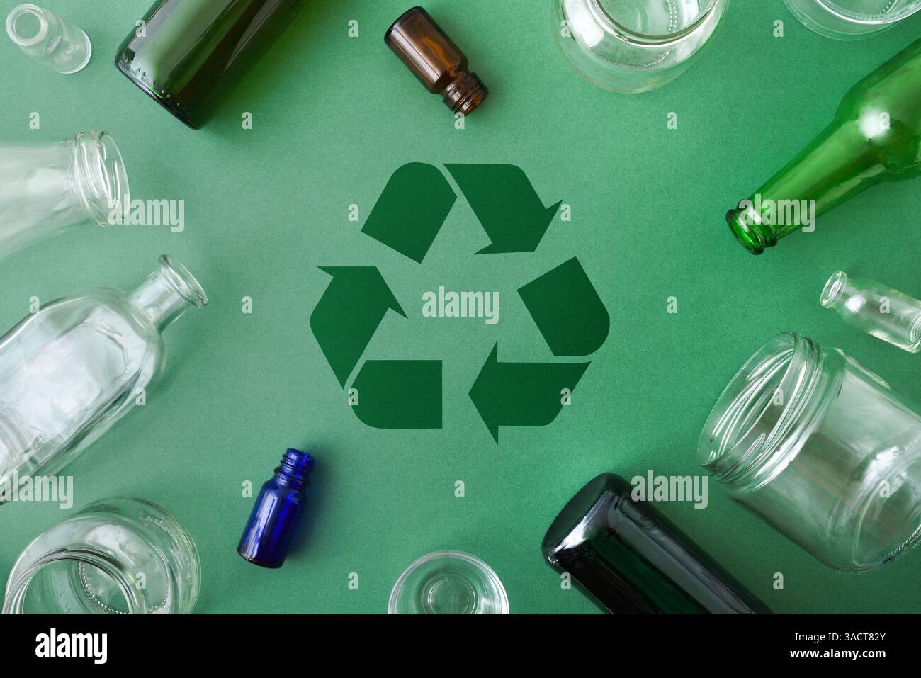 Concetto di inquinamento e riciclaggio del vetro con simbolo di riciclaggio al centro di una base verde e contenitori di vetro intorno. Vista dall'alto. Foto Stock