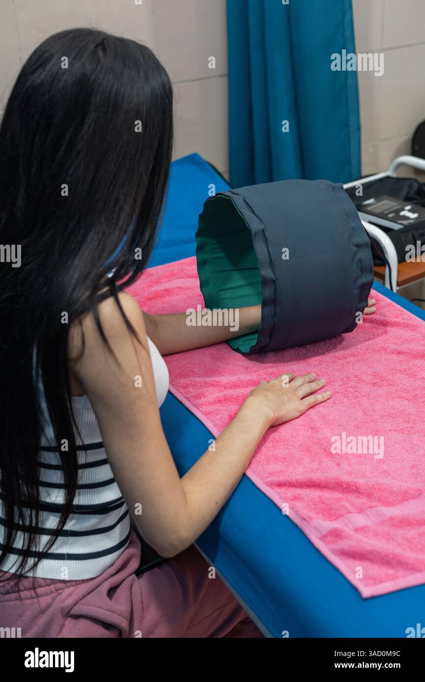 In una clinica tranquilla, una giovane donna prova la terapia magnetica, inseguendo sollievo e speranza con ogni minuto silenzioso sotto il dispositivo di guarigione. Foto Stock