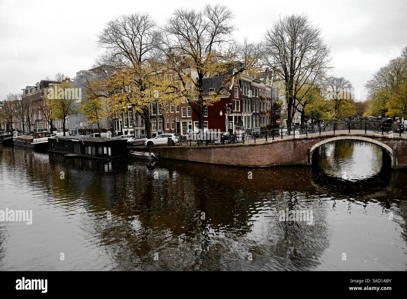 Gli iconici canali di Amsterdam Binnenstad risplendono sotto ponti storici, incorniciati da affascinanti case dai tetti spioventi, barche, vegetazione lussureggiante e vivace vita cittadina Foto Stock