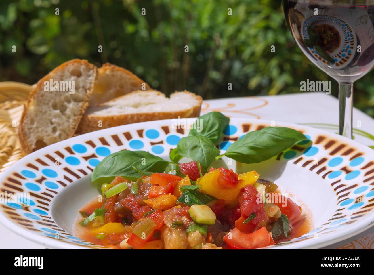 Ratatouille con baguette e vino rosso in un ambiente estivo all'aperto Foto Stock