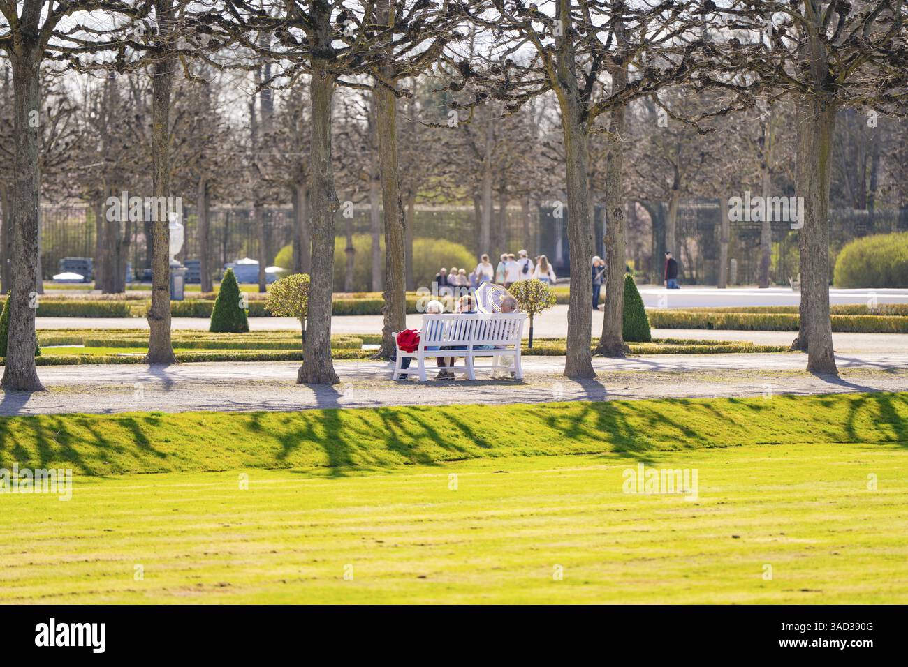 Persone su una panchina di un parco in un viale ombreggiato. Scena primaverile con ombra e prati, giardini del Palazzo di Schwetzingen, Germania, Europa Foto Stock