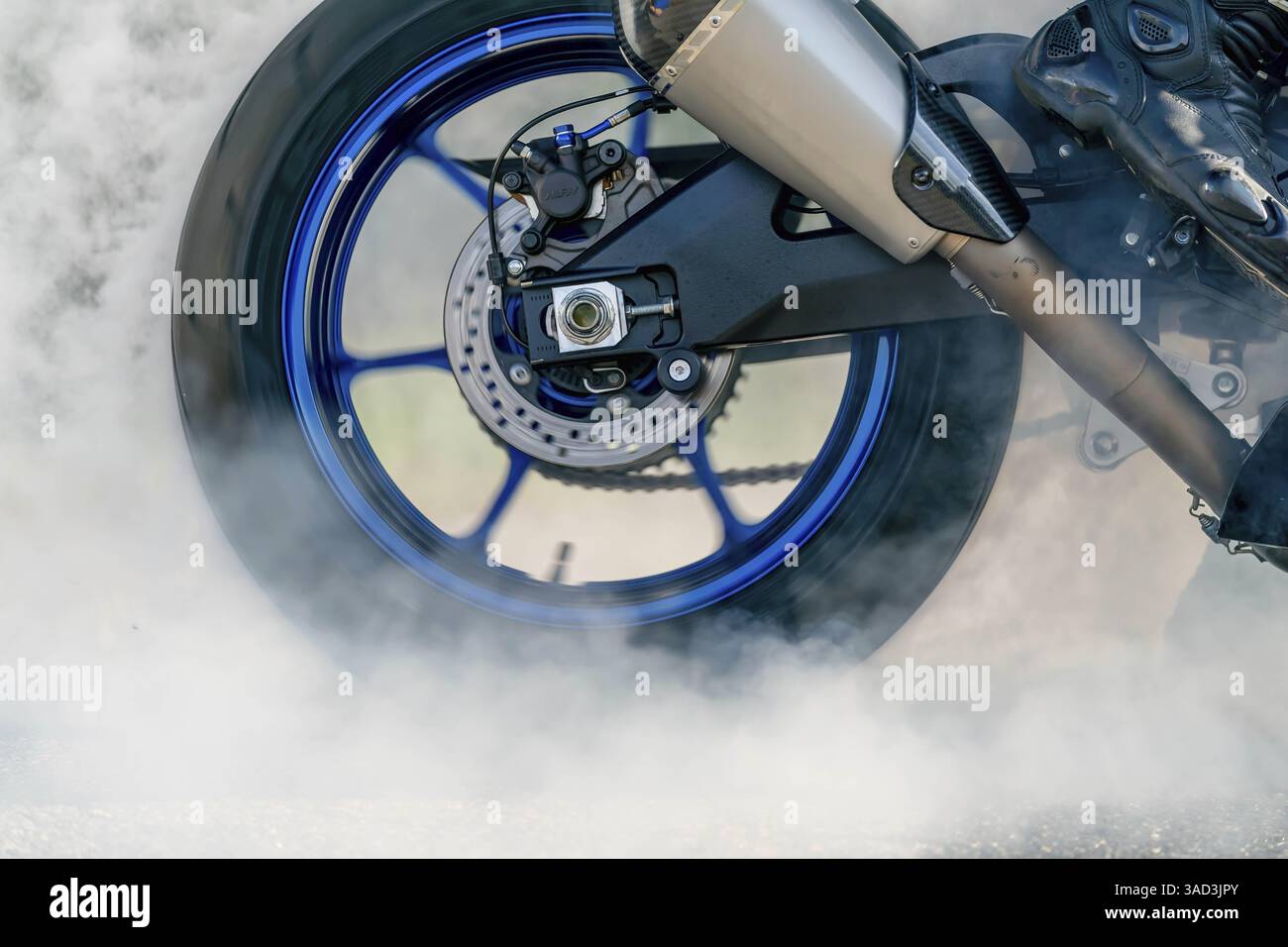 Un motociclista supera la linea rossa, afferrando il manubrio mentre la ruota posteriore gira selvaggiamente. Il fumo ondeggia dalla parte posteriore, arricciandosi verso l'alto, mentre regge Foto Stock