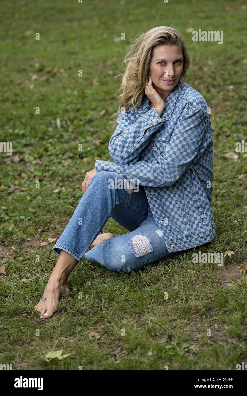 Un bellissimo modello biondo gode del sole di fine estate all'aperto. Circondata da vegetazione lussureggiante e luce soffusa del sole, irradia calore ed eleganza nella S Foto Stock