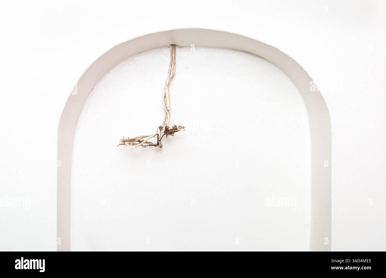 Vecchio cavo elettrico esposto a parete. Filo sbriciolato bianco in una nicchia ad arco. Concetto per fili abbandonati, incendi elettrici, pericoli per la sicurezza o. Foto Stock