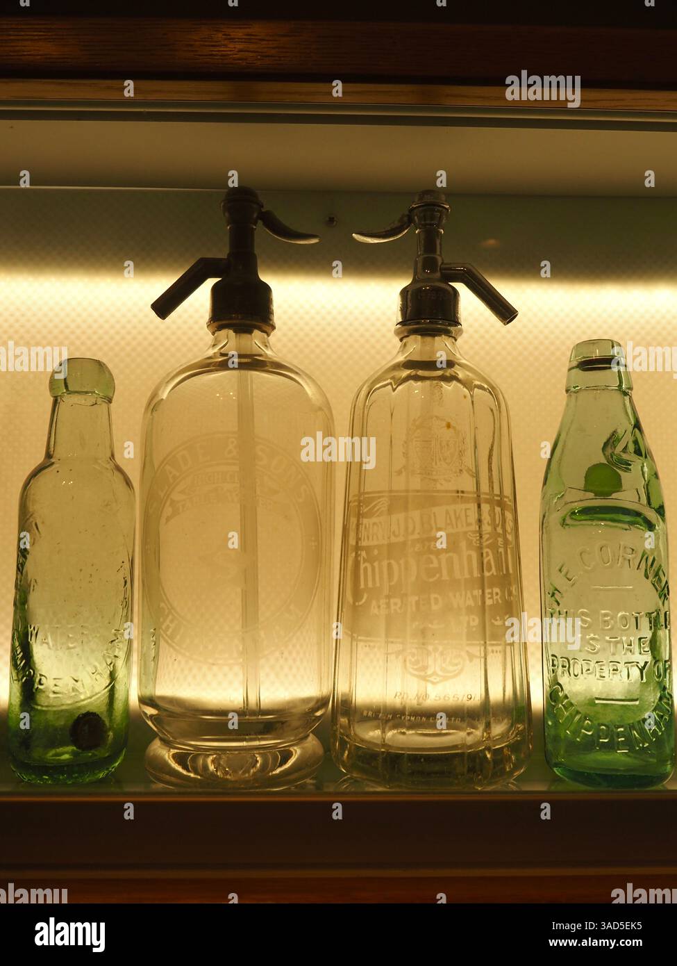 Selezione di bottiglie di vetro vintage non alcoliche o analcoliche recanti il nome del produttore, in particolare A J Taylor di Chippenham. Retroilluminato nella custodia del display. Foto Stock