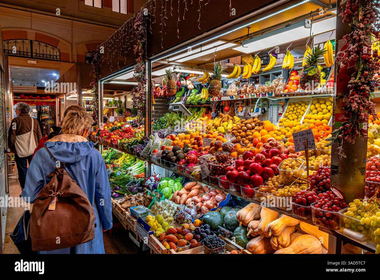 Persone che fanno acquisti di frutta e verdura in una stalla all'interno del mercato delle Erbe, un grande mercato coperto nel centro storico di Bologna, Italia Foto Stock